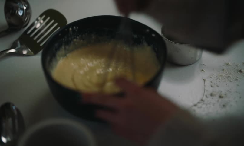 A persons hand stirring a utensil in a black bowl of yellow food