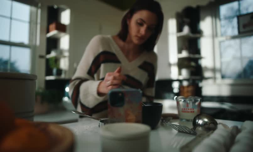 Woman cooking in a pan on the stove and interacting with a smartphone in front of her