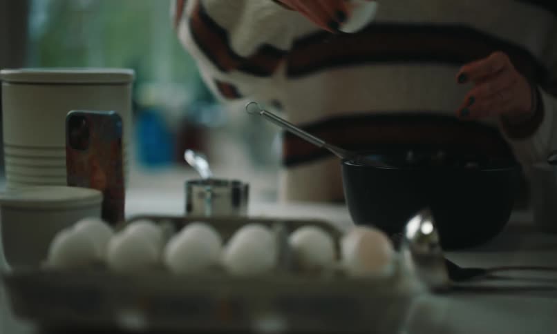 A person wearing a striped sweater is breaking eggs and whisking on her kitchen counter
