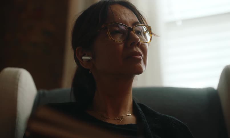 A woman wearing glasses sitting in a comfortable chair closes her book and picks up a smartphone