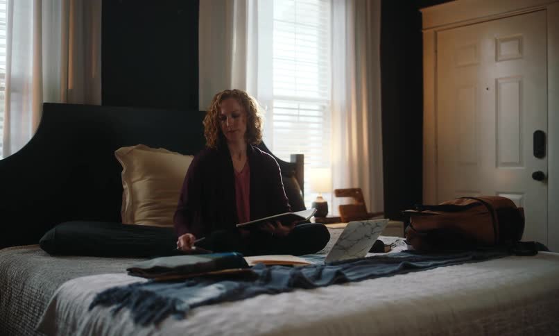 A woman is writing and using a laptop in bed