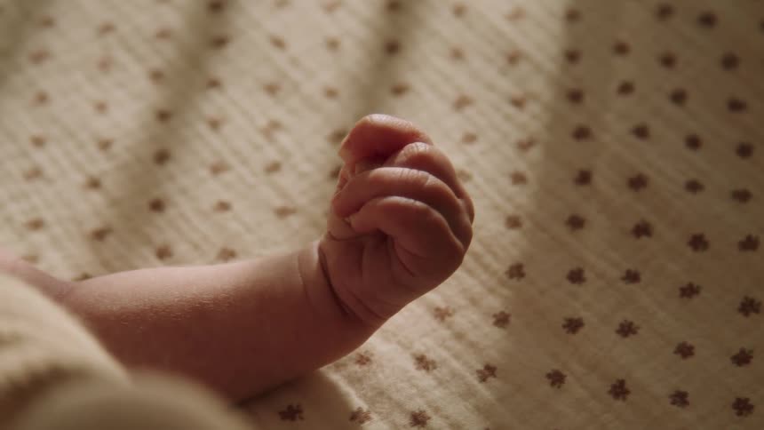 A newborn baby is clenching his fist while lying on a white linen sheet