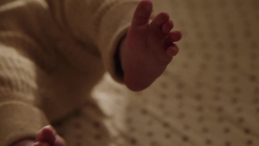 The tiny foot of a baby wearing a knitted outfit resting on a soft patterned surface