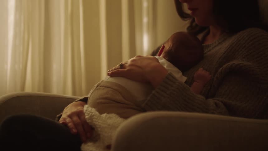 Mother strokes her child while cuddling the infant and rocking in a chair