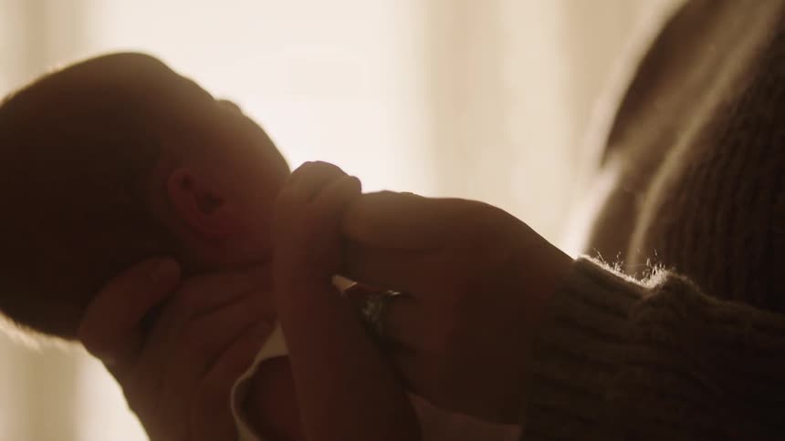 Mother strokes the hand of her baby while standing near the window with her child