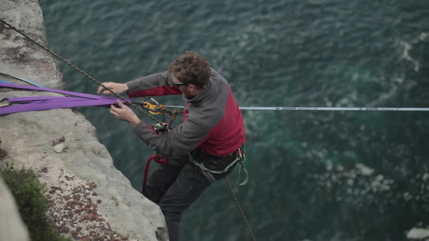 A man adjusting zip line equipment on an ocean-side cliff