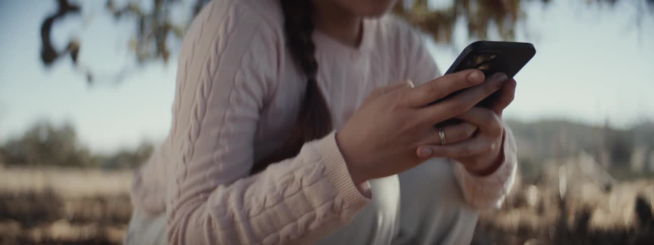 Woman crouched beneath a tree typing on a cell phone