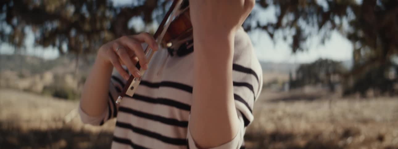 Woman playing violin in a field surrounded by trees