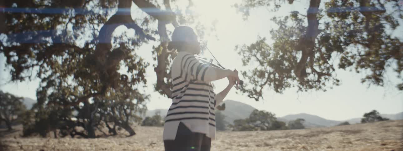 A woman is playing the violin under the bright sun