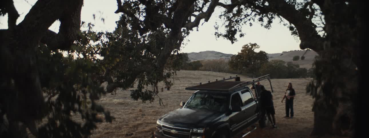 Some people around a pickup truck in the middle of a field in the late afternoon