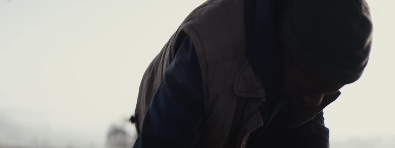 A man with bags stands up from the ground in a field to continue his journey