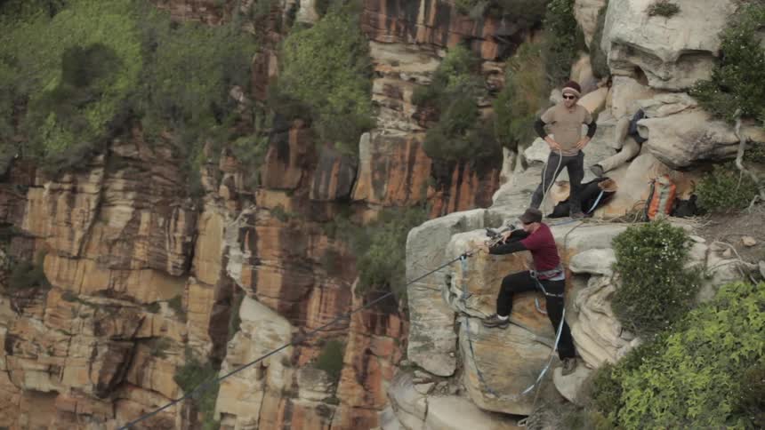 Man secures a zip line between two cliffs on a sunny day