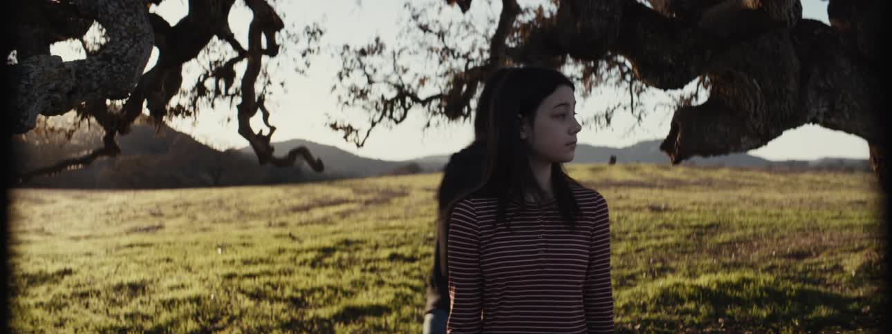 Girl picking up a leaf from a tree and walking while another girl runs after her