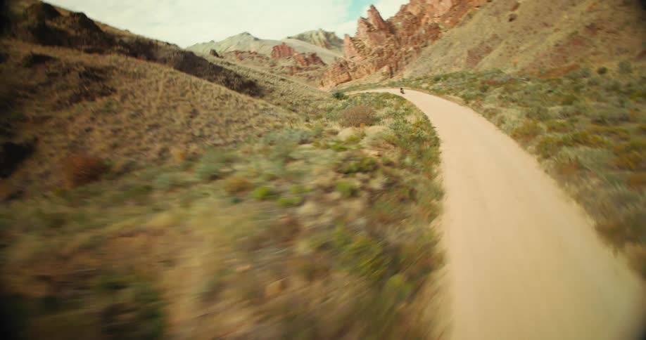 Person on a motorcycle traveling on a narrow dirt road surrounded by mountains