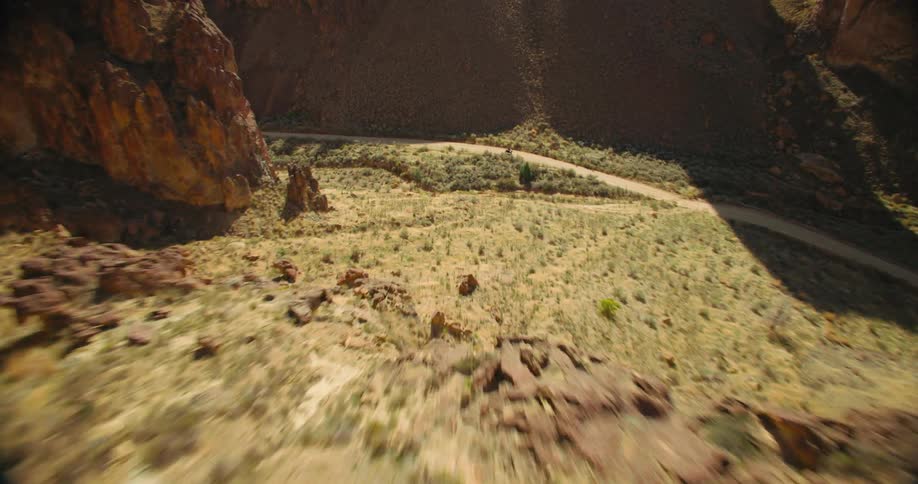 A low angle drone shot sweeps over a desert landscape towards a motorcycle traversing a dirt road between rocky hills