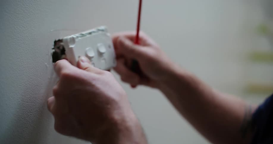 A person is installing or repairing an electrical outlet holding the outlet with one hand and using a screwdriver with the other hand to connect or secure the wiring