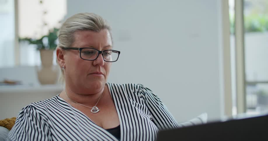 The face of a woman wearing glasses who is intently fiddling with something in front of her while sitting