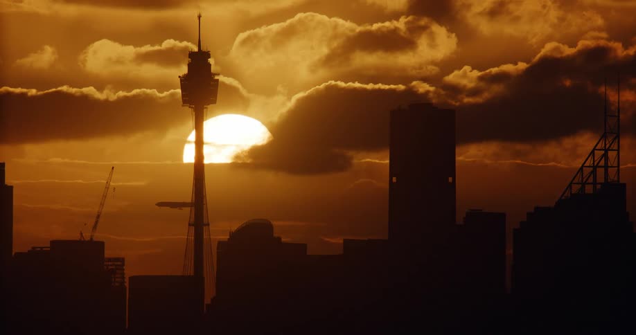 Airplane flies through the red tinted sky above the city as the sun sets