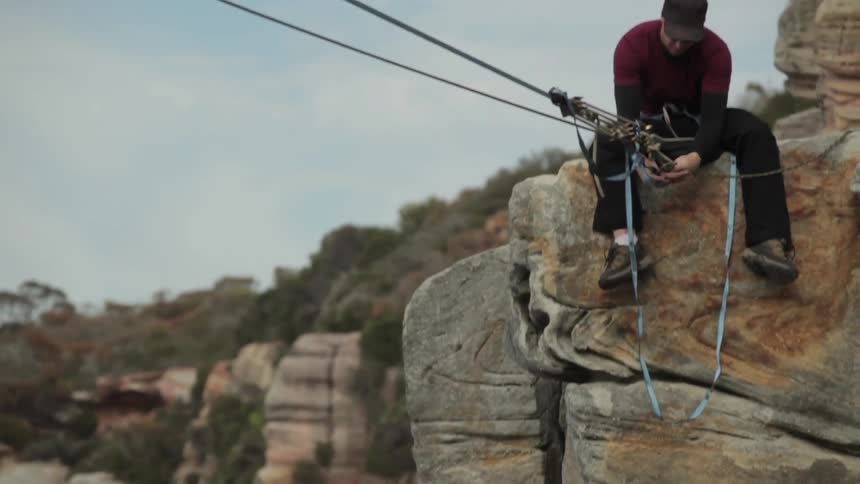 Man sitting and setting up a tight rope on a cliff