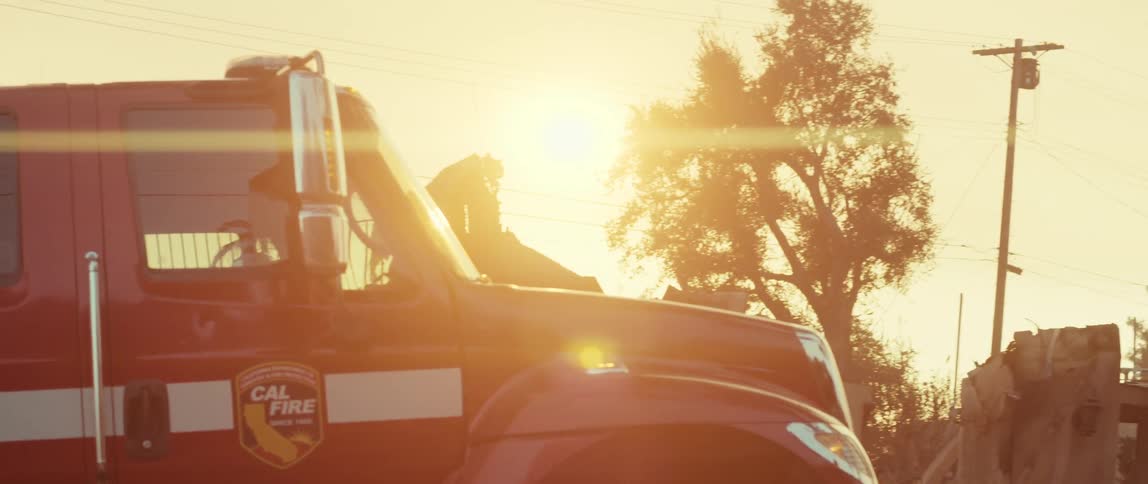 Sun shines from a red tinted sky onto a cal fire truck parked near a burnt building