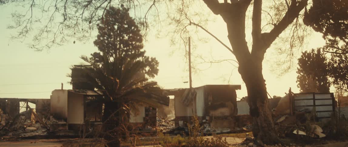 A house that is partially destroyed and there are several trees in front on an orange day