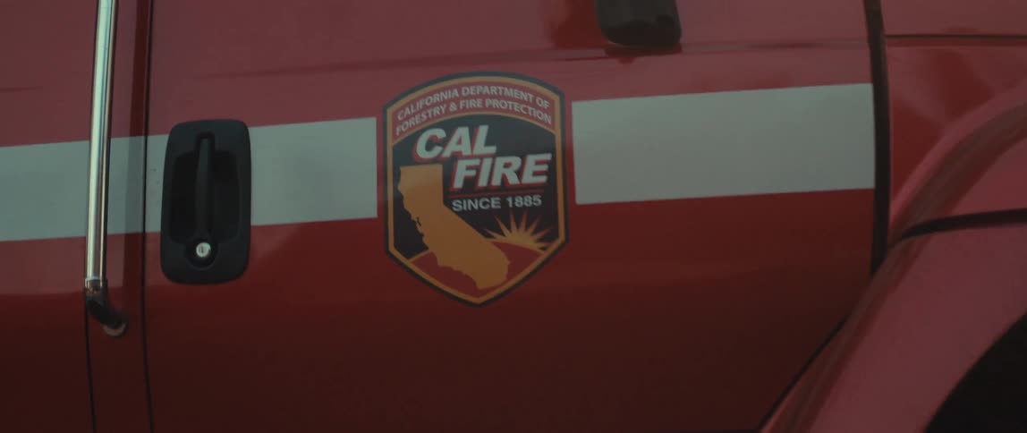 A closeup shot of a red fire truck shows the cal fire emblem at sunset