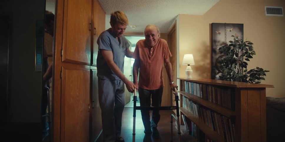 Nurse helping an elderly patient walk with a walker down the hallway of the house