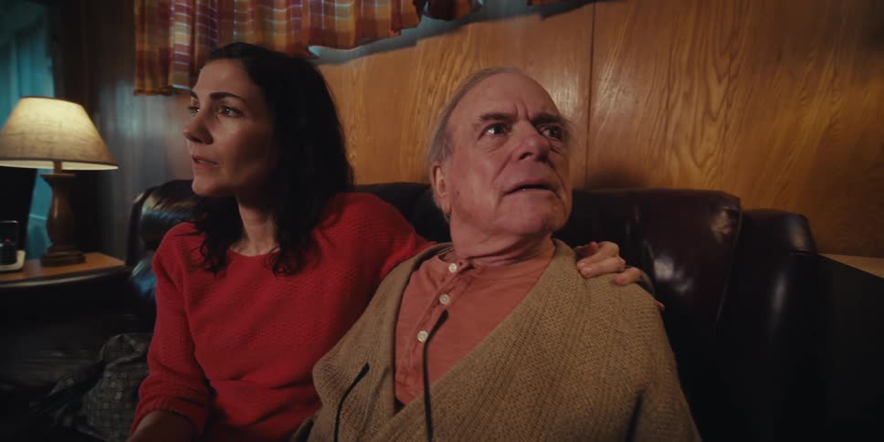 Adult daughter sitting cuddled next to elderly father on living room sofa