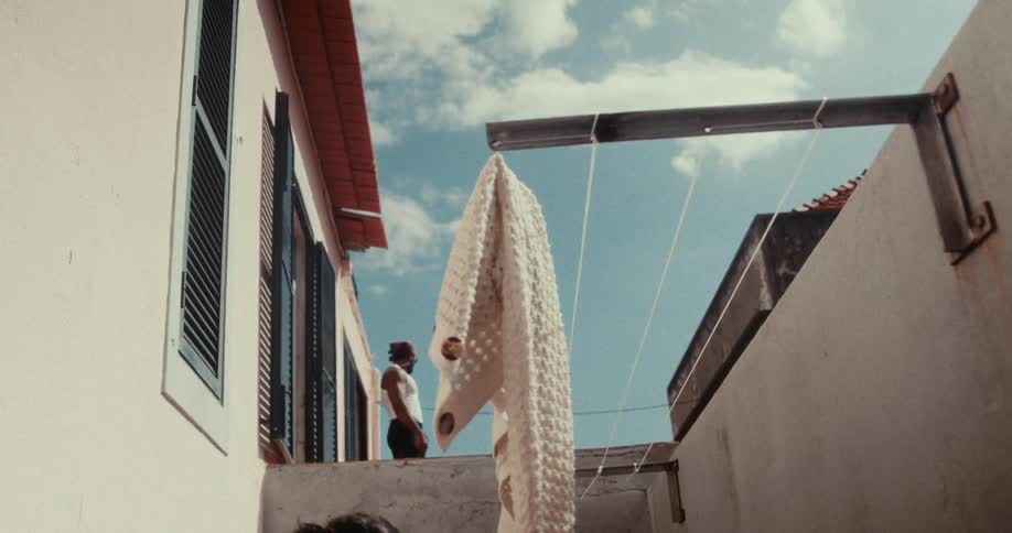 Man on the porch of a house and a woman in the foreground next to a clothesline