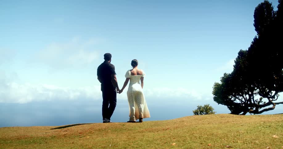 Couple back to back and holding hands on a hill