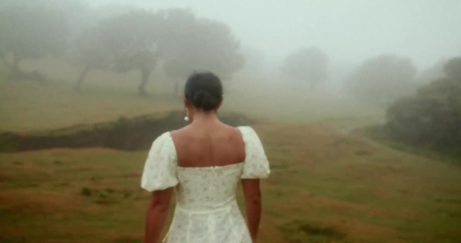 Woman from behind walking in a white dress in a foggy field