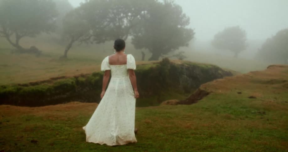 Woman in a long white dress walking in a foggy natural area