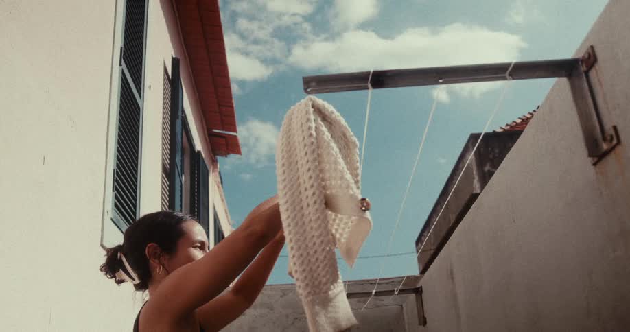A woman hanging clothes on a clothesline at home under a blue sky
