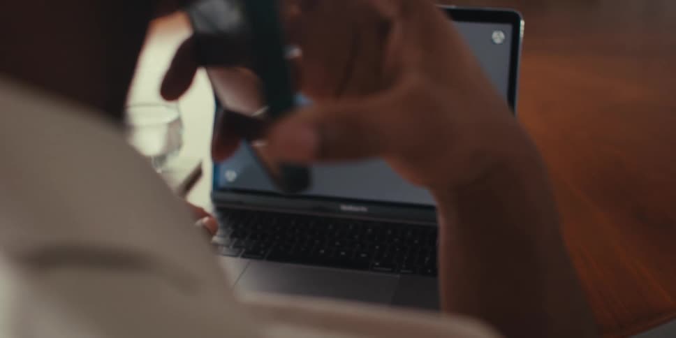 Hand answering a call on a smartphone and then typing on a laptop