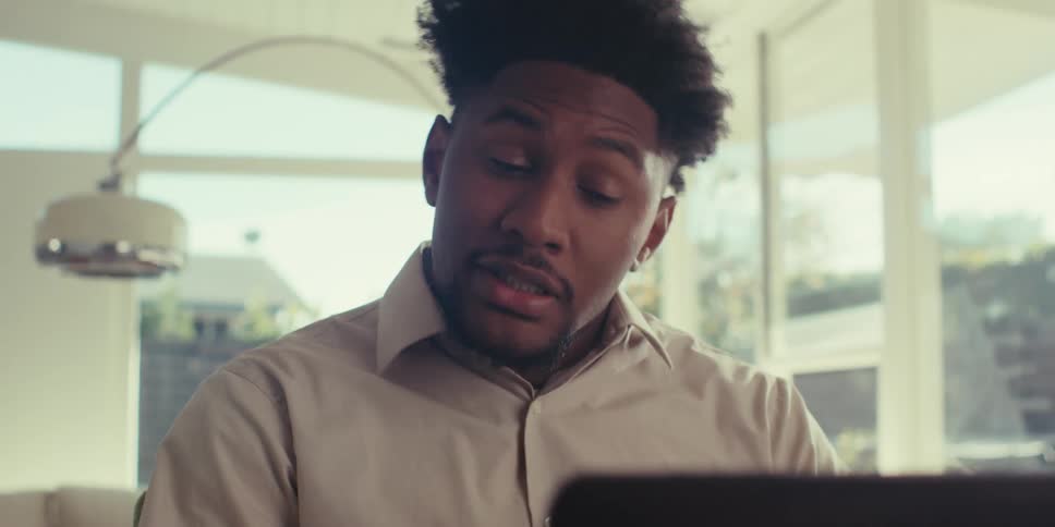 A man in a brown shirt holds a video call on his laptop in the living room