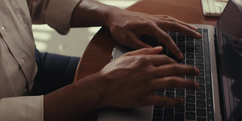 A person is typing on a laptop keyboard at a wooden table