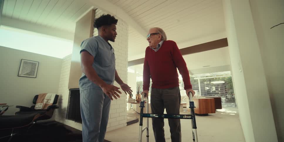 Young man accompanying elderly gentleman down hallway of house