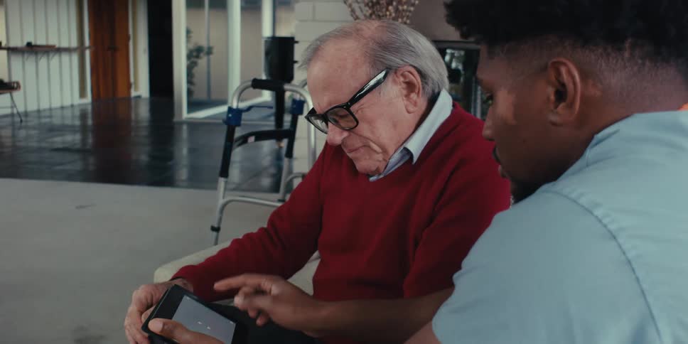 A home healthcare worker is helping a patient by showing him a tablet