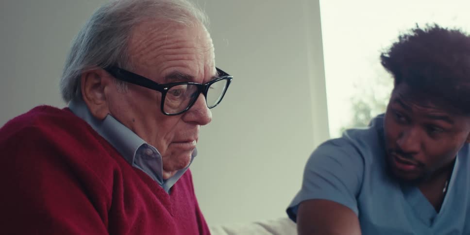 Elderly patient sitting and talking to a nurse next to him