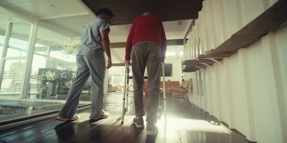 Nurse escorting an elderly man down a hallway