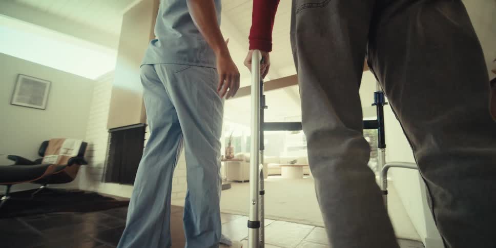 A nurse talks and walks with a man using a walker