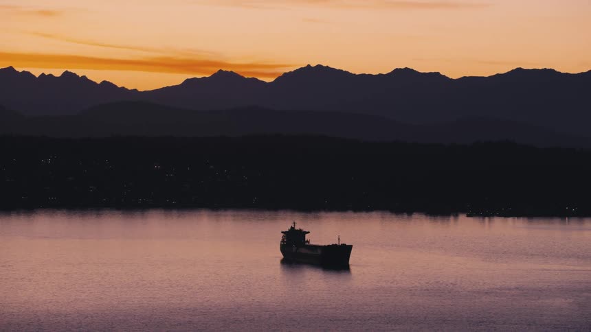 Aerial view of a boat on a calm sea with the silhouette of mountains around