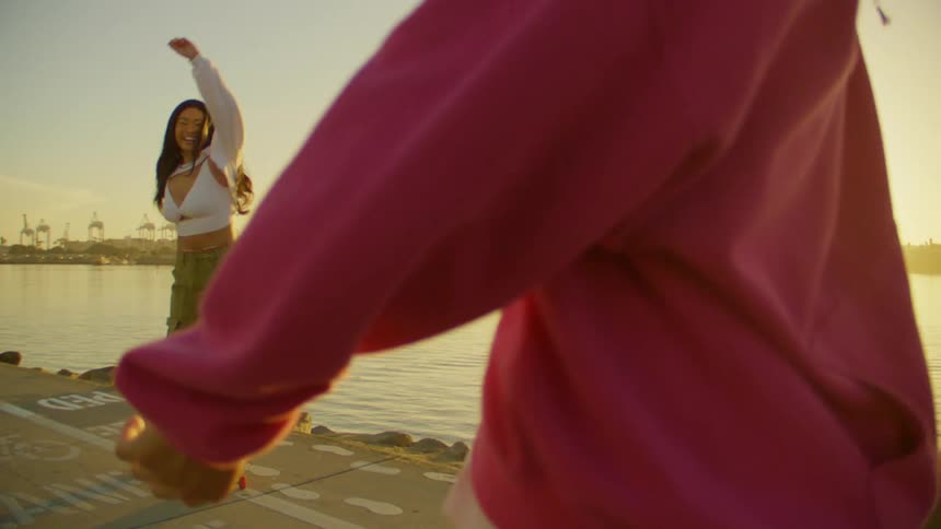 A couple of dancers perform energetic dance moves on roller blades near a waterfront at sunset