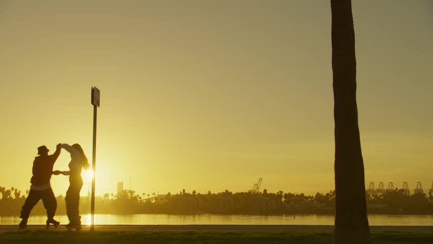 Silhouette of a man and a woman dancing hand in hand while roller skating along a lake