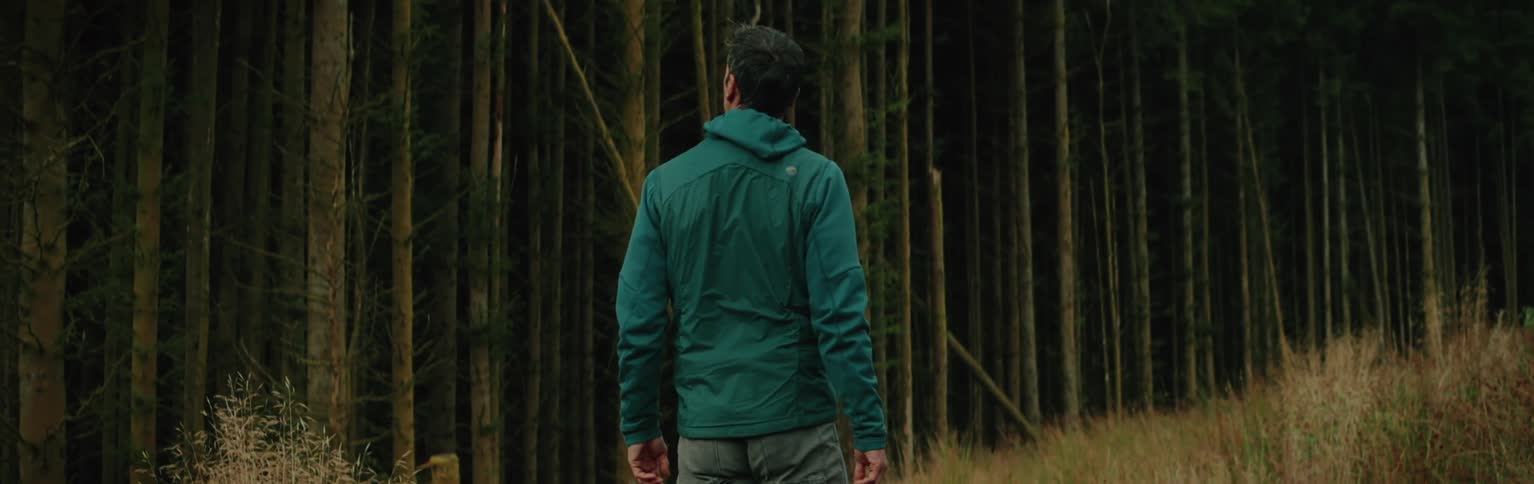 Man walking through a field stops to looks at the nearby woods