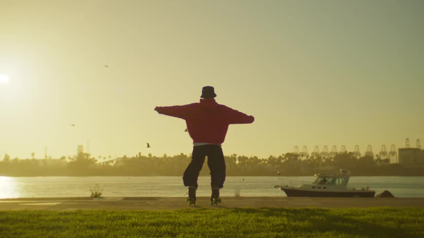 A person is roller skating on a paved surface near a body of water with palm trees in the background during sunset