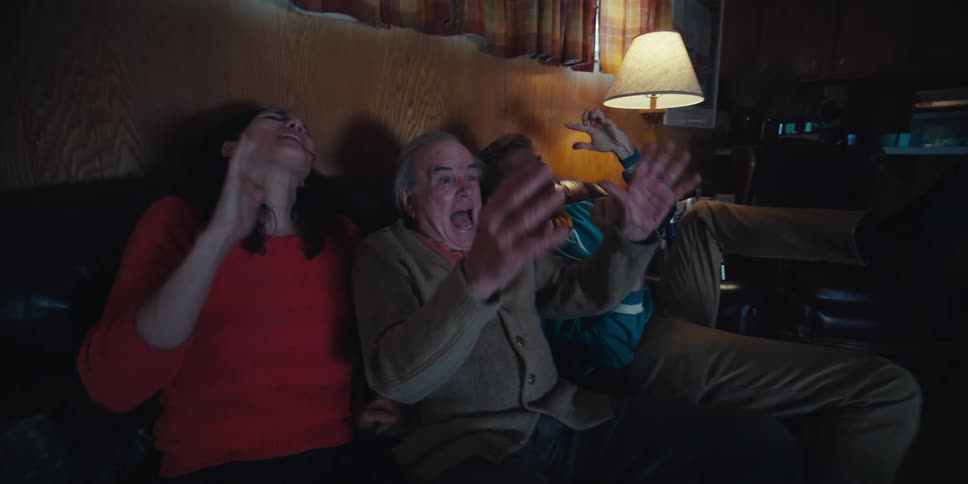 Elderly man and two young adults sitting on sofa cheering in living room