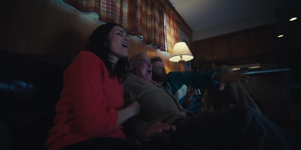 Elderly father sitting with all his two adult children on the couch watching something in the living room