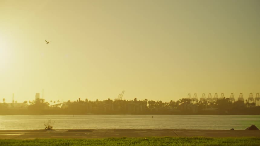 A hazy golden sunset illuminates a cityscape silhouette along a distant shoreline