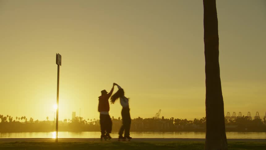 Man and woman holding hands dancing on roller skates by a lake